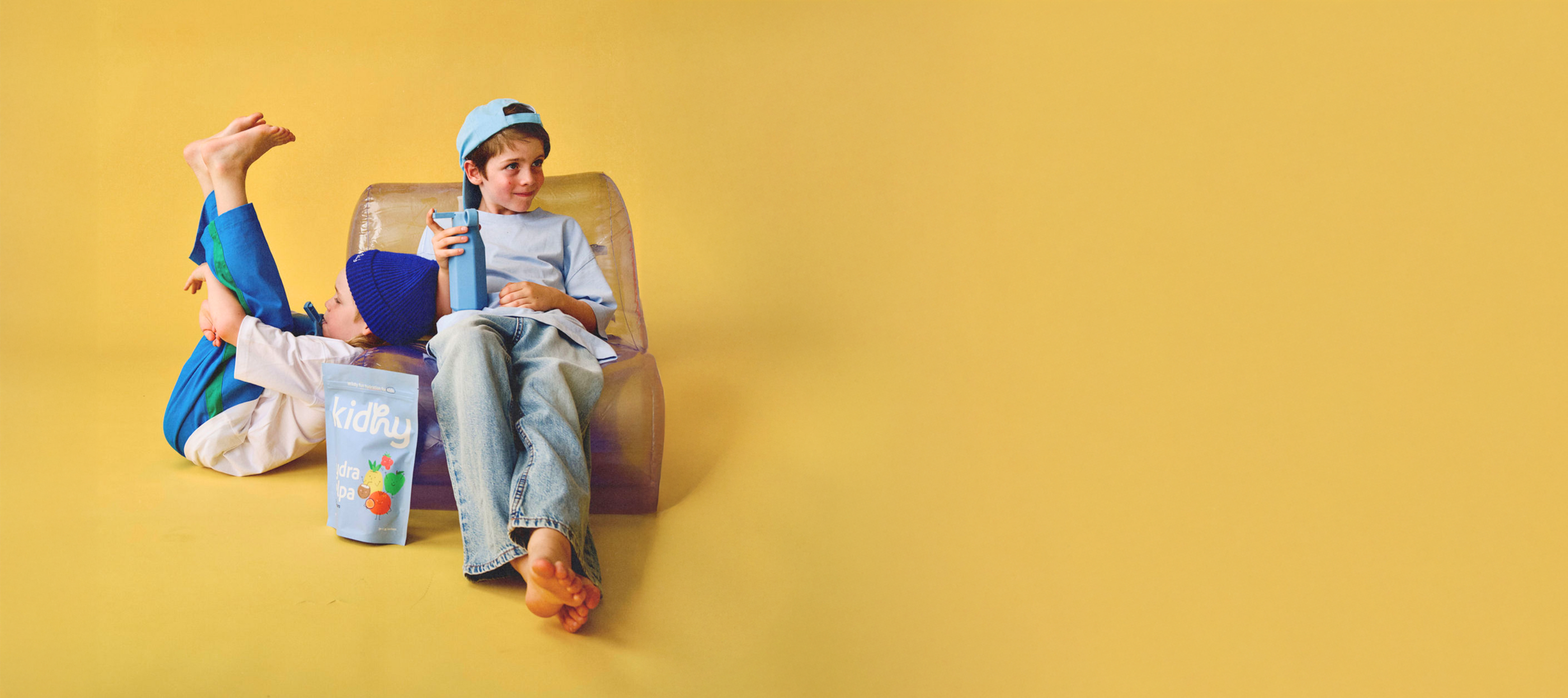 young kids relaxing on a chair with kidhy hydration drink packet and kidhy drink bottle