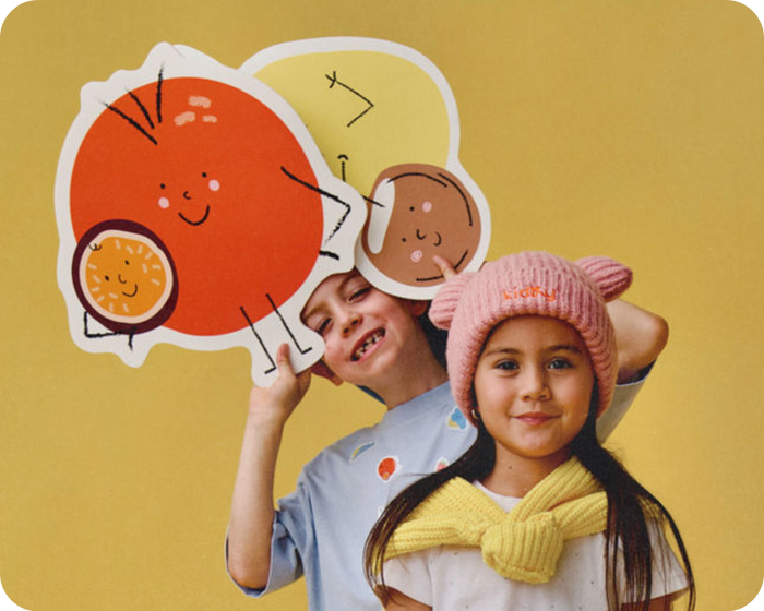 2 kids in front of yellow background 1 is holding giant pictures of fruit, kidhy hydration drinks for kids